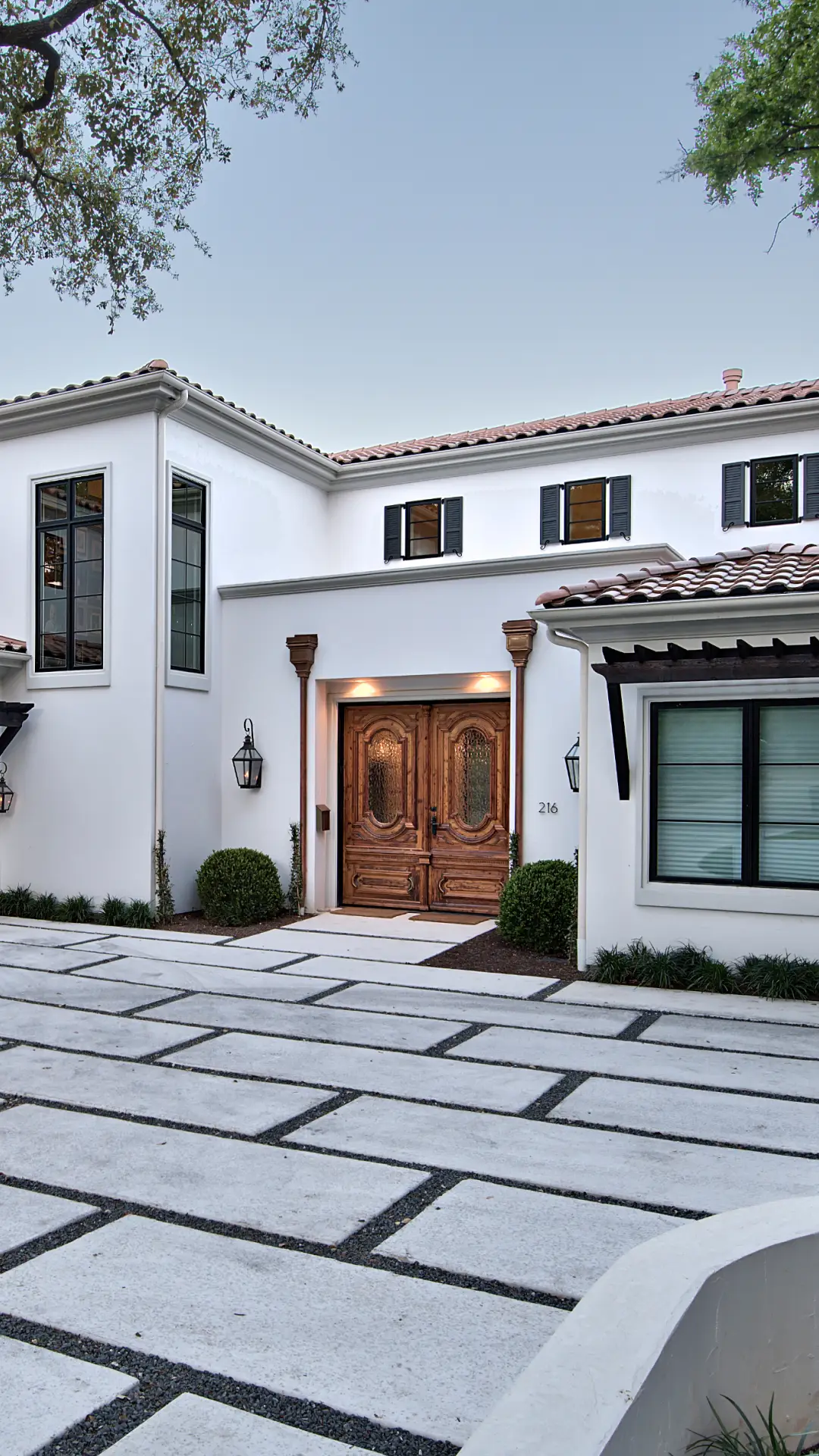 White Mediterranean-style custom home with clay tile roof, carved wood entry doors and a paver driveway