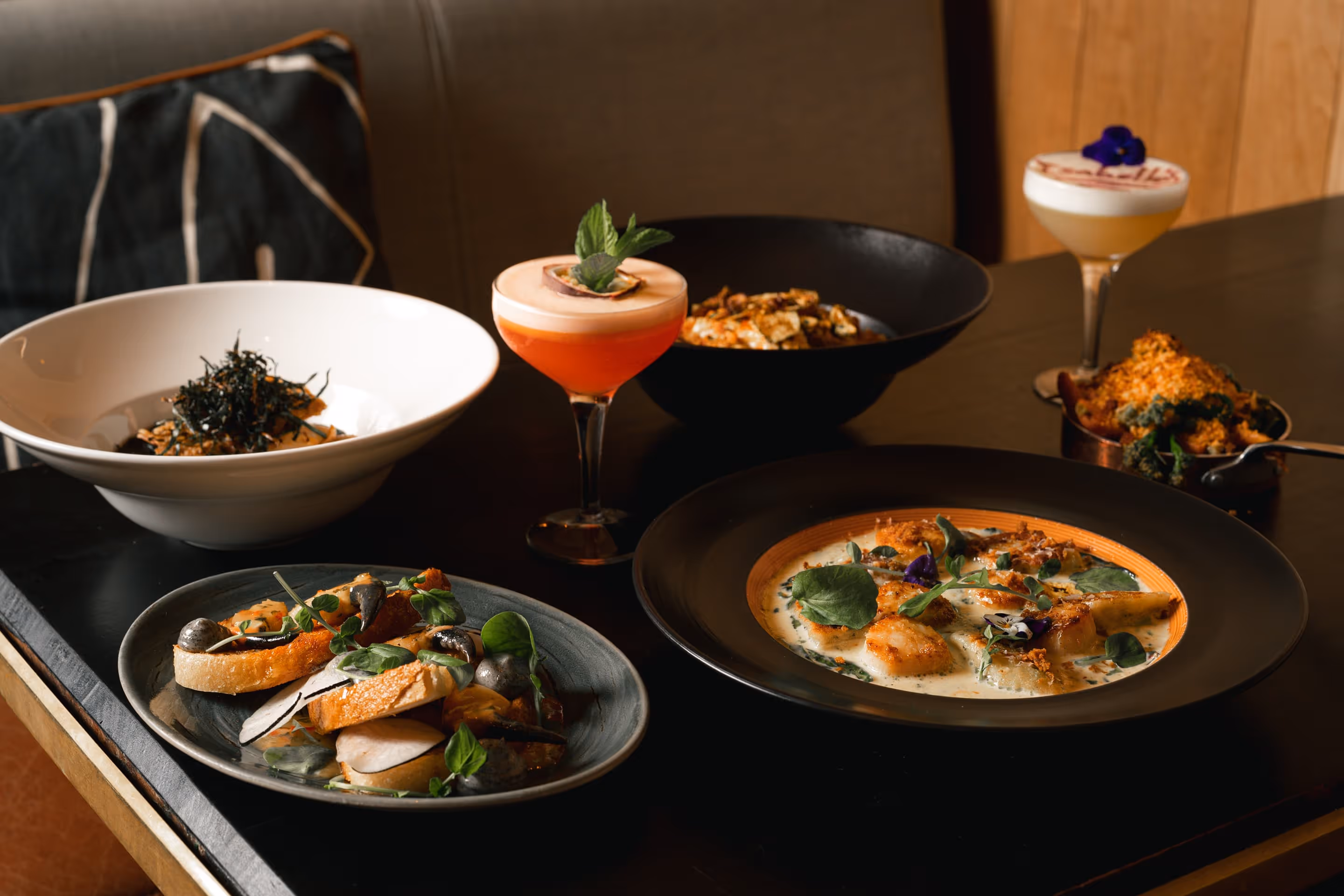 Upscale restaurant interior with red leather booths, glass pendant lights, and greenery on walls.