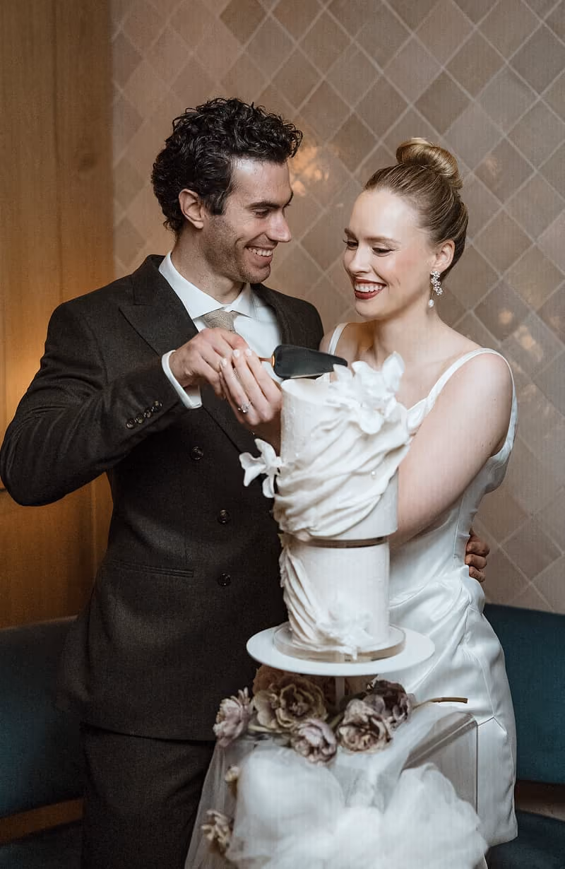 Smiling bride and groom cutting a white wedding cake with floral decorations.