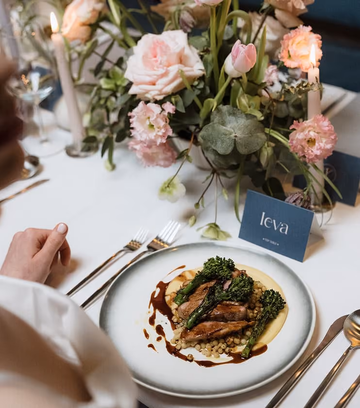 A plated course served beside blush roses on a wedding table.