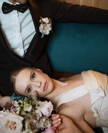 A bride resting against her partner, holding a bouquet of blush roses.