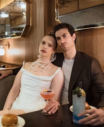 A bride and groom sharing cocktails at a candlelit table.