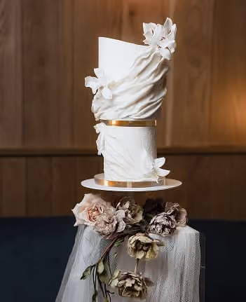 A tiered white wedding cake finished with a gold band and dried flowers.