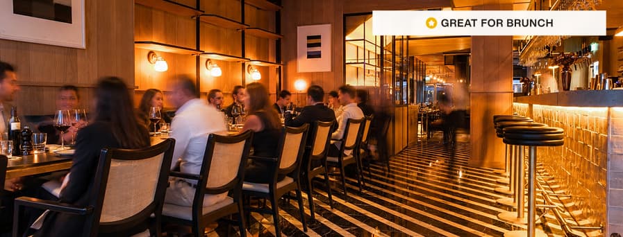 Stylish restaurant interior with red booths, round tables, hanging lights, and modern art on walls.