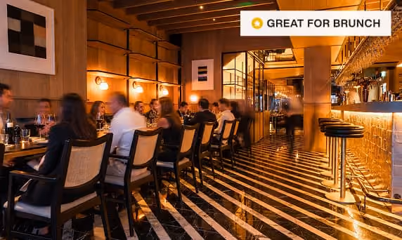 Stylish restaurant interior with red booths, round tables, hanging lights, and modern art on walls.