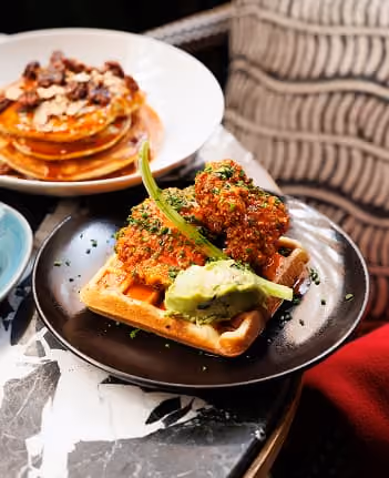 Waffle topped with fried chicken, green pepper, and a dollop of green sauce on a black plate.