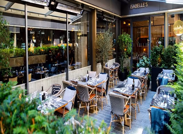Terrace tables set for group dining, framed by planting and the restaurant's glass frontage.