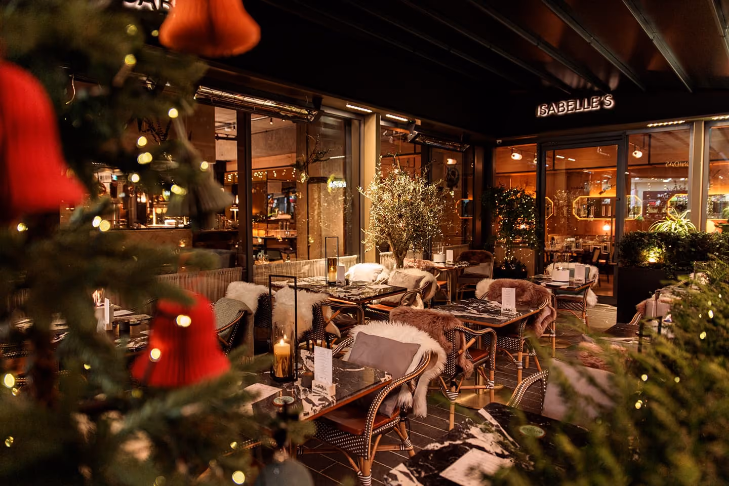 Cozy restaurant terrace with marble tables, fur-covered chairs, candles, and Christmas tree ornaments.