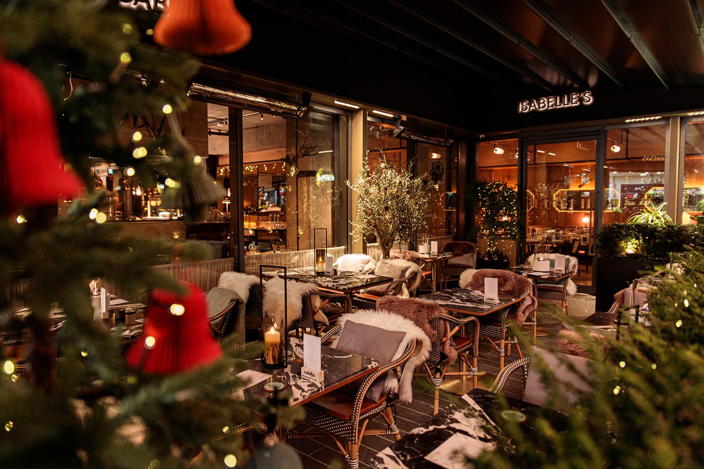 Cozy restaurant terrace with marble tables, fur-covered chairs, candles, and Christmas tree ornaments.