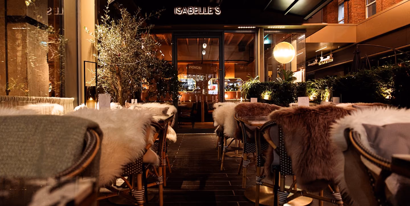 Outdoor restaurant seating with cozy fur-covered chairs and warm ambient lighting at night.
