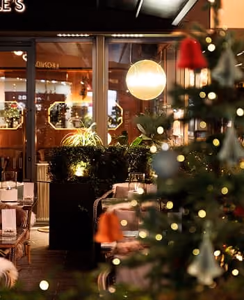 Indoor cafe seating area with warm lighting and blurred Christmas tree in foreground.