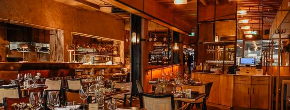 Stylish restaurant interior with red booths, round tables, hanging lights, and modern art on walls.