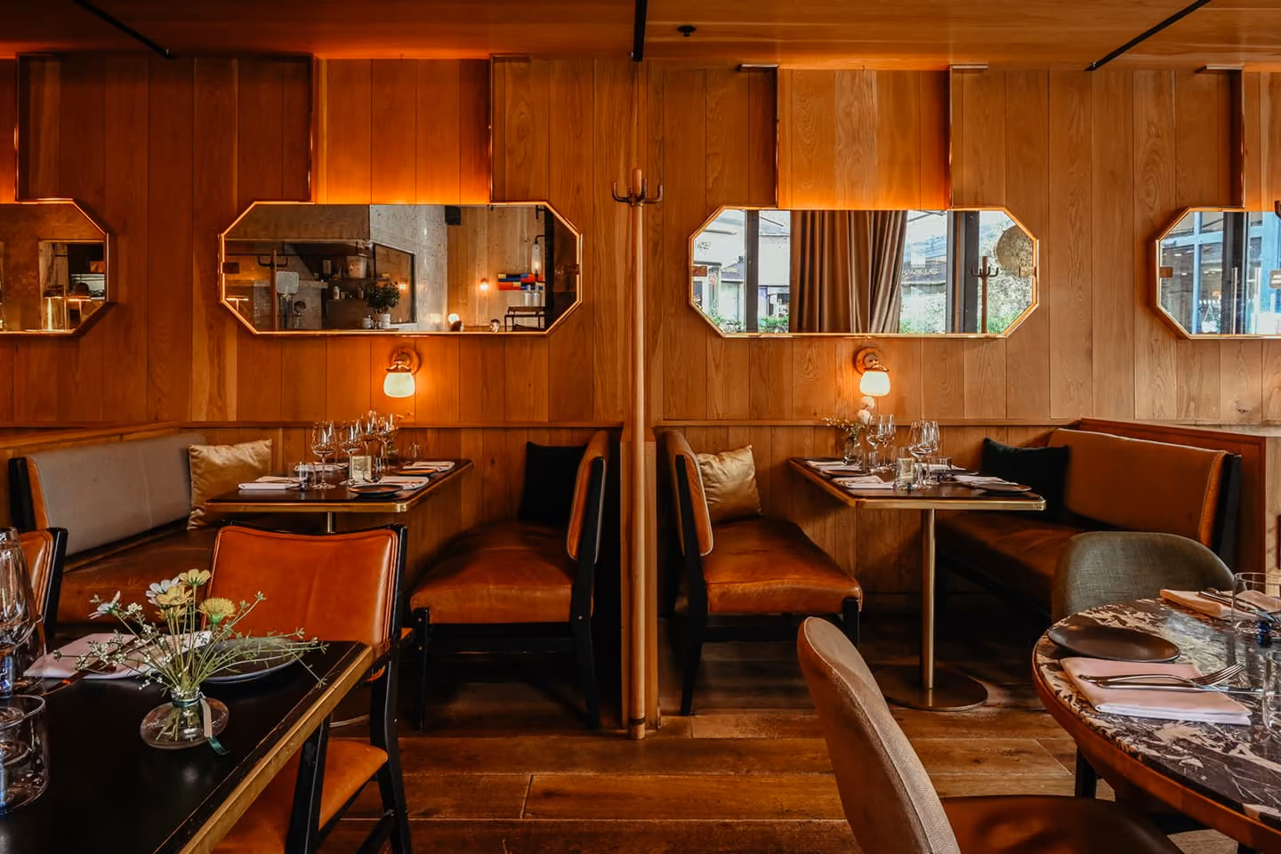 Upscale restaurant interior with red leather booths, glass pendant lights, and greenery on walls.