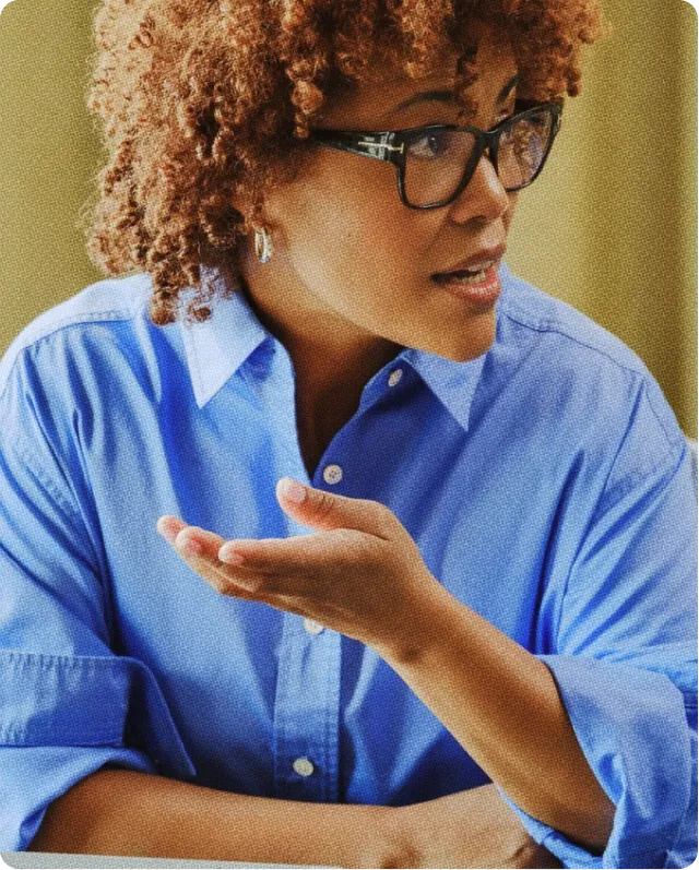 Femme à lunettes en chemise bleue parlant et gesticulant avec la main droite levée.