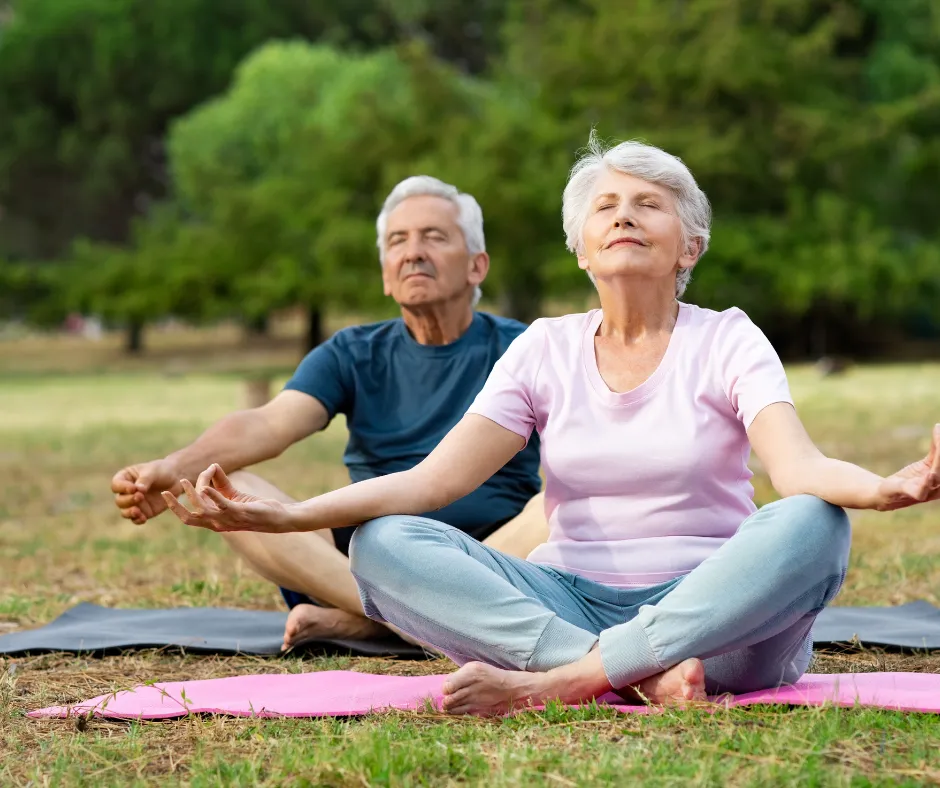An older couple meditating together outdoors on a sunlit lawn