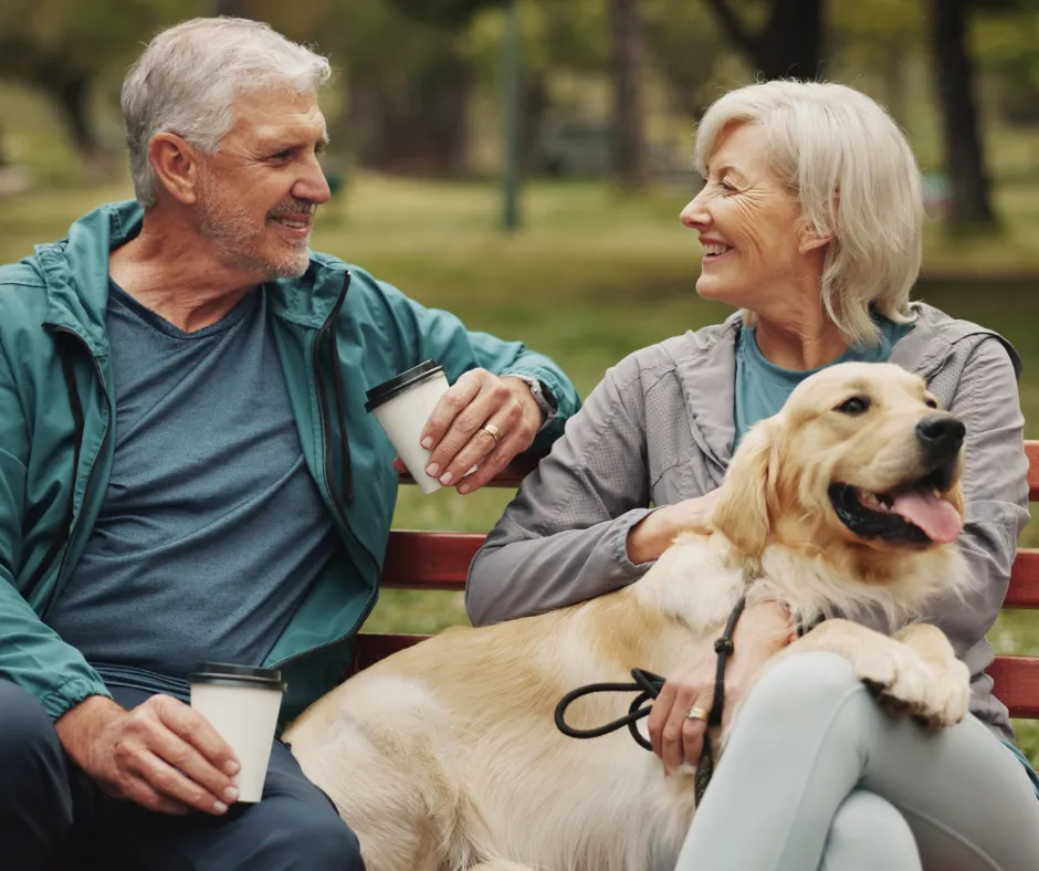 A couple relaxing with their dog and coffee on a park bench