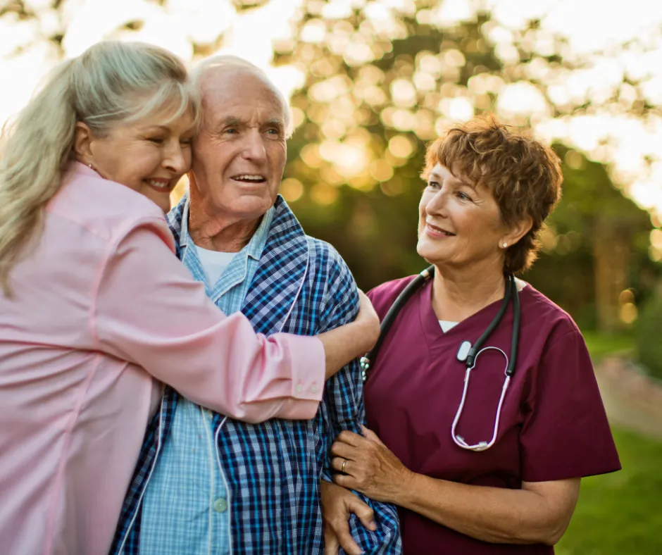 A caregiver beside a couple in a garden at sunset