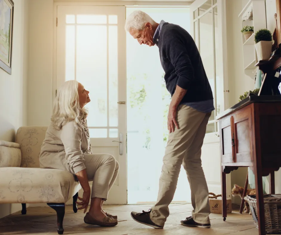 A man gently helping a seated woman in a sunlit living room