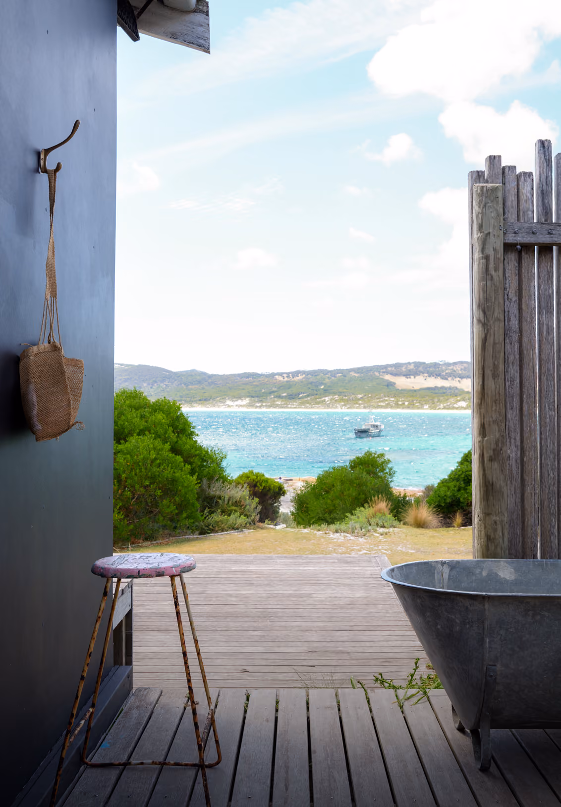 View of turquoise sea and hills seen through an open wooden deck with stool and metal tub.
