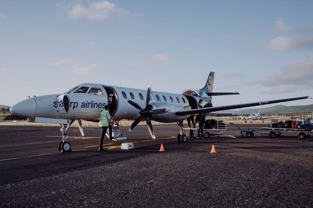 Sharp Airlines plane on tarmac with people loading luggage under clear sky.
