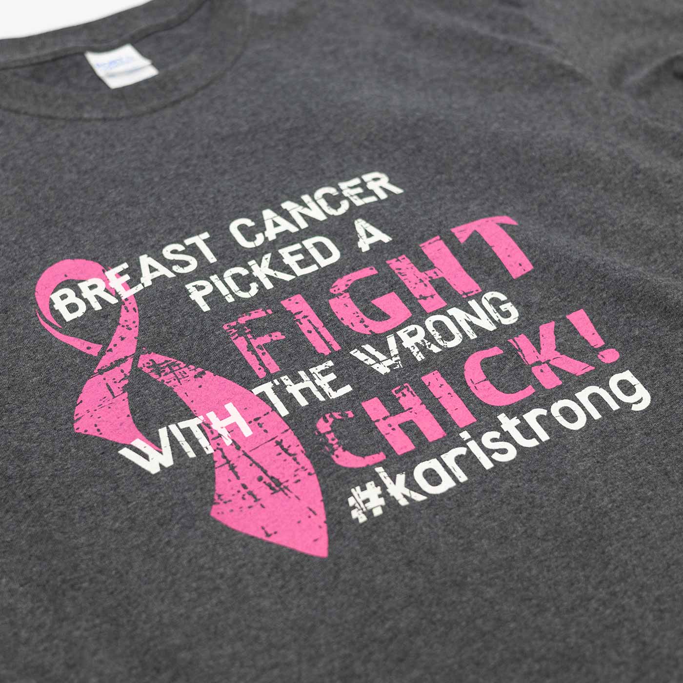 Dark gray T-shirt with a pink breast cancer awareness ribbon and text that reads 'Breast cancer picked a fight with the wrong chick! #karistrong' in white and pink letters.