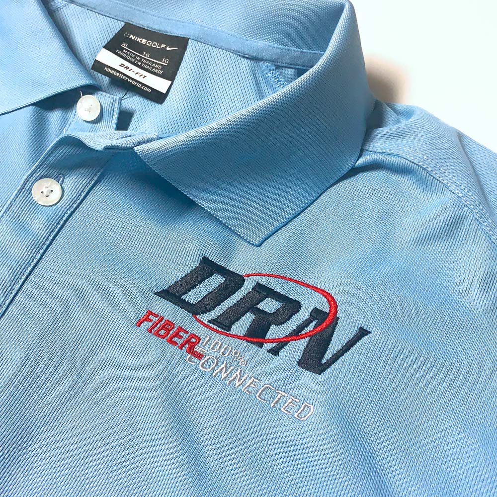 Light blue Nike Golf polo shirt with white buttons, featuring an embroidered logo on the chest reading 'DRN FIBER 100% CONNECTED' with a red swirl around the letters DRN.