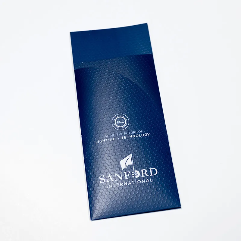 Dark blue bubble-padded mailer envelope with white text and logos reading 'EMC Leading the Future of Lighting + Technology' and 'Sanford International' with a flag logo.