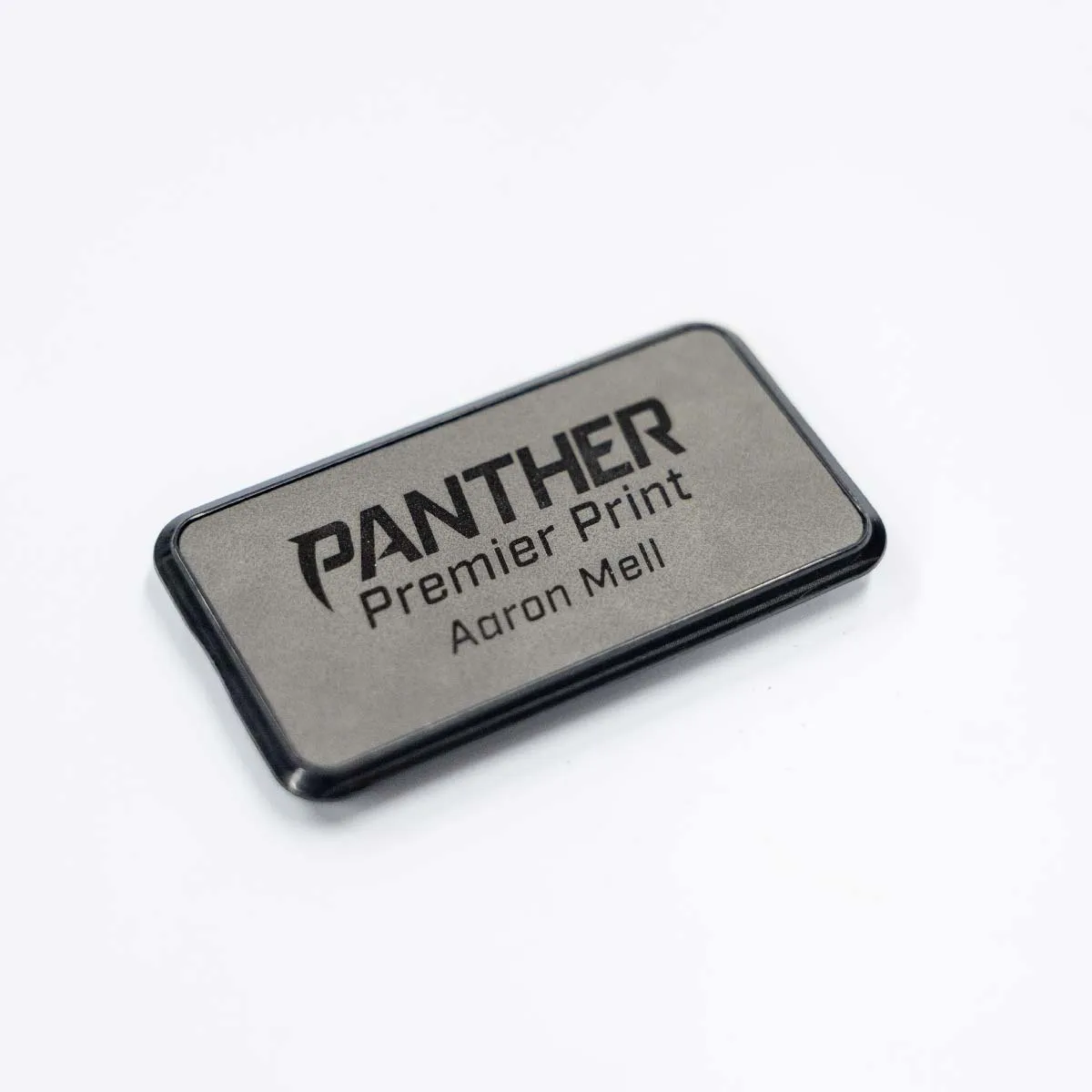 Rectangular gray name tag with black border displaying the text 'PANTHER Premier Print Aaron Mell' on a white background.