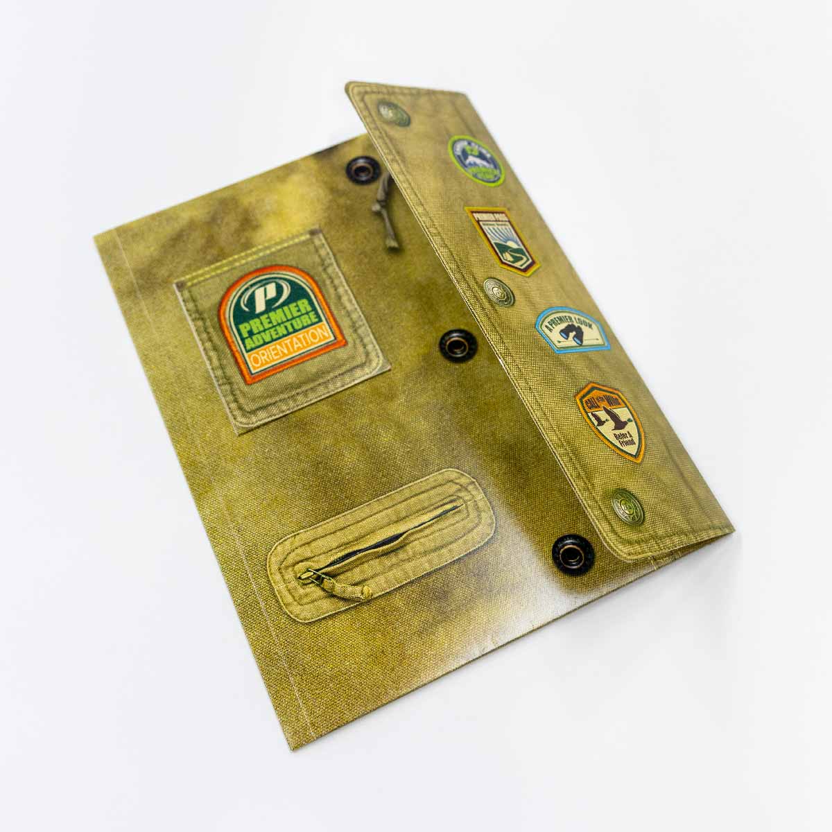 A khaki colored folder designed to look like a rugged fabric jacket with a zipper pocket, snap buttons, and patches including one that says Premier Adventure Orientation and others with outdoor adventure themes.