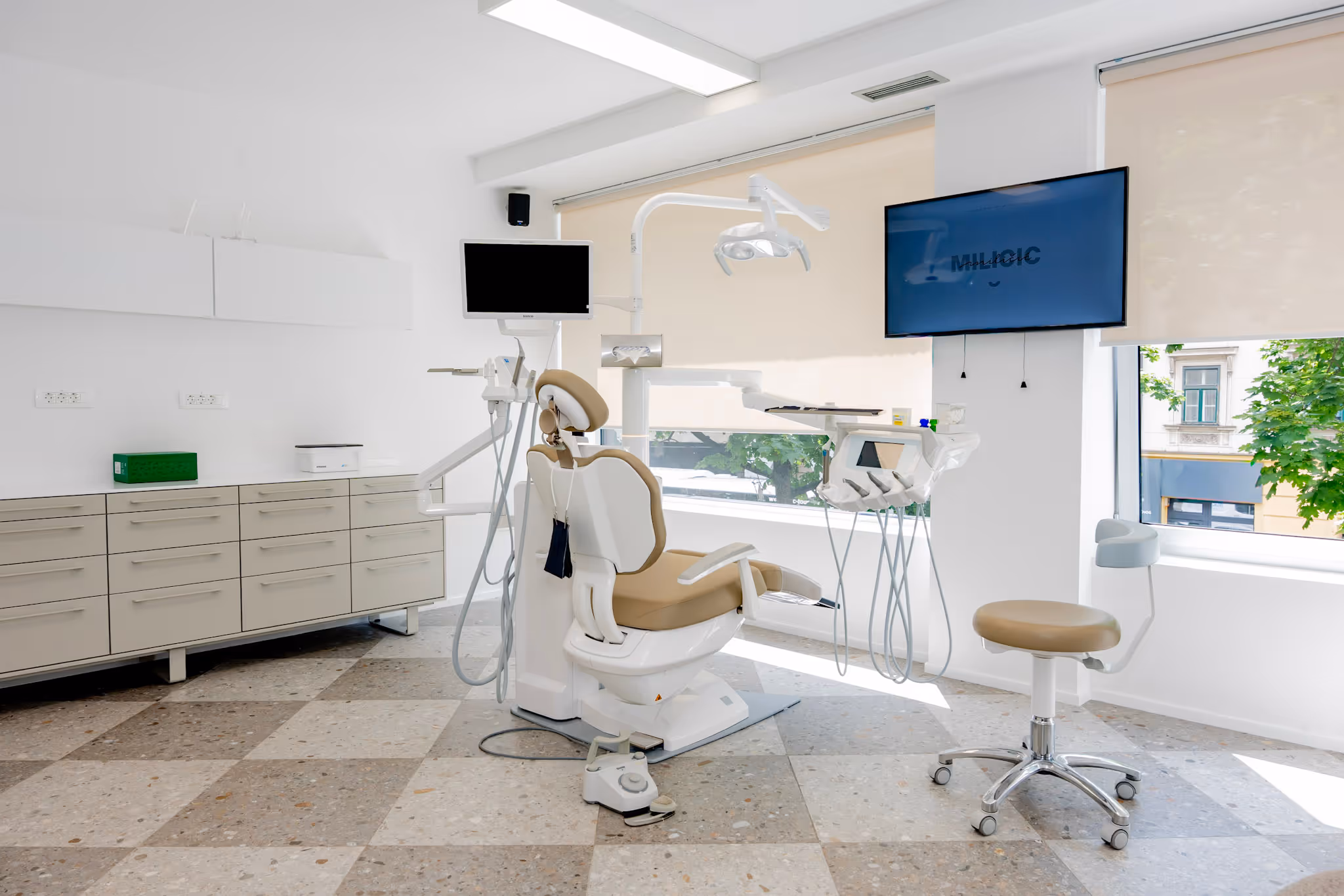 Moderna stomatološka ordinacija s dentalnom stolicom, instrumentima i monitorima kraj prozora.