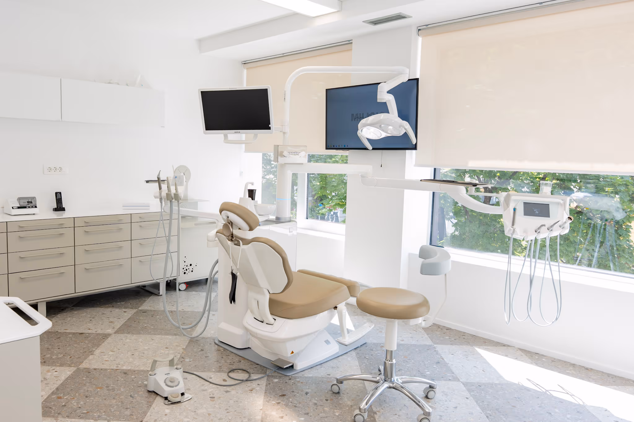 Moderna stomatološka ordinacija s dentalnom stolicom, instrumentima i monitorima kraj prozora.