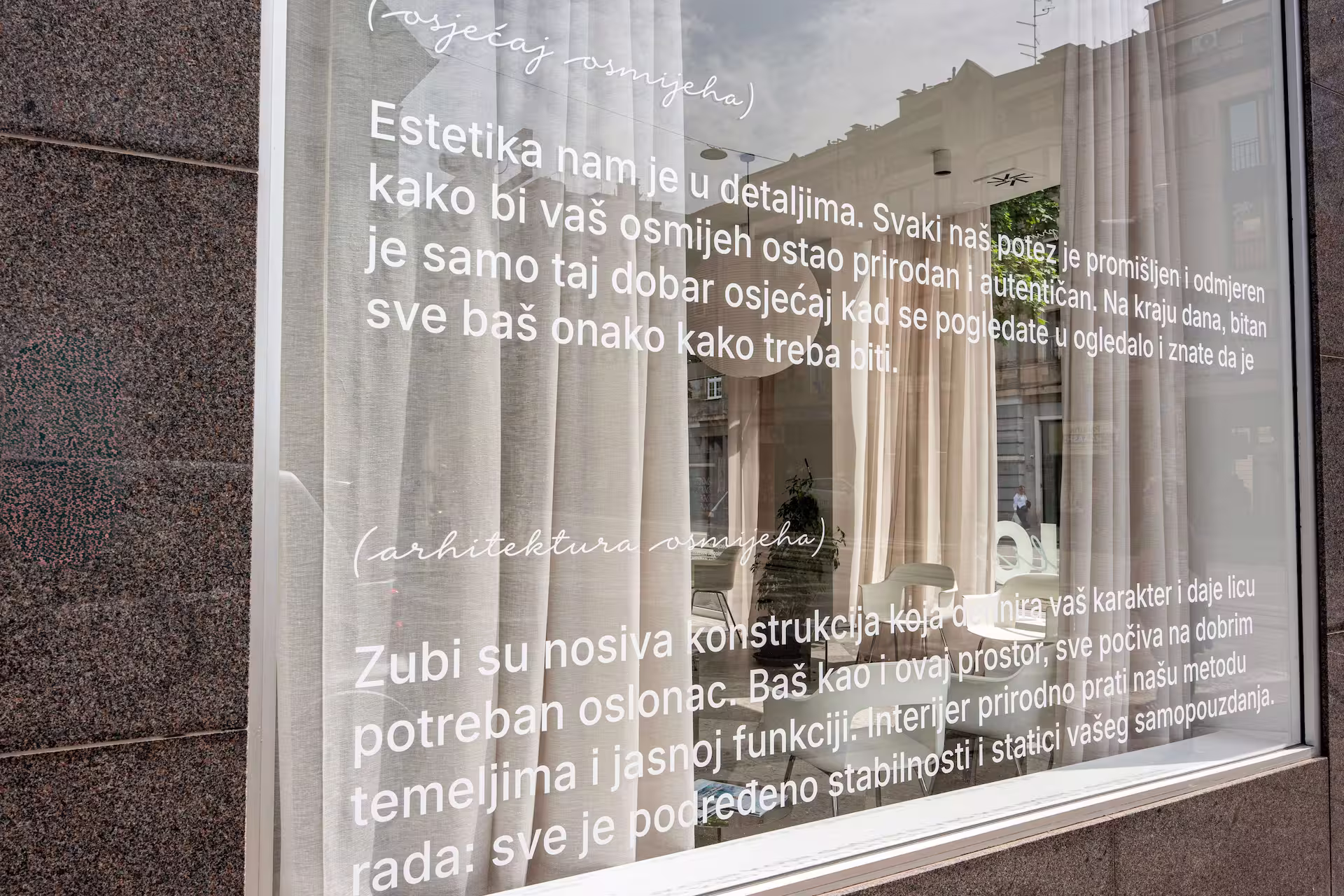 Stakleni izlog s natpisom na hrvatskom jeziku o estetici i arhitekturi osmijeha, s uvidom u unutarnji prostor.
