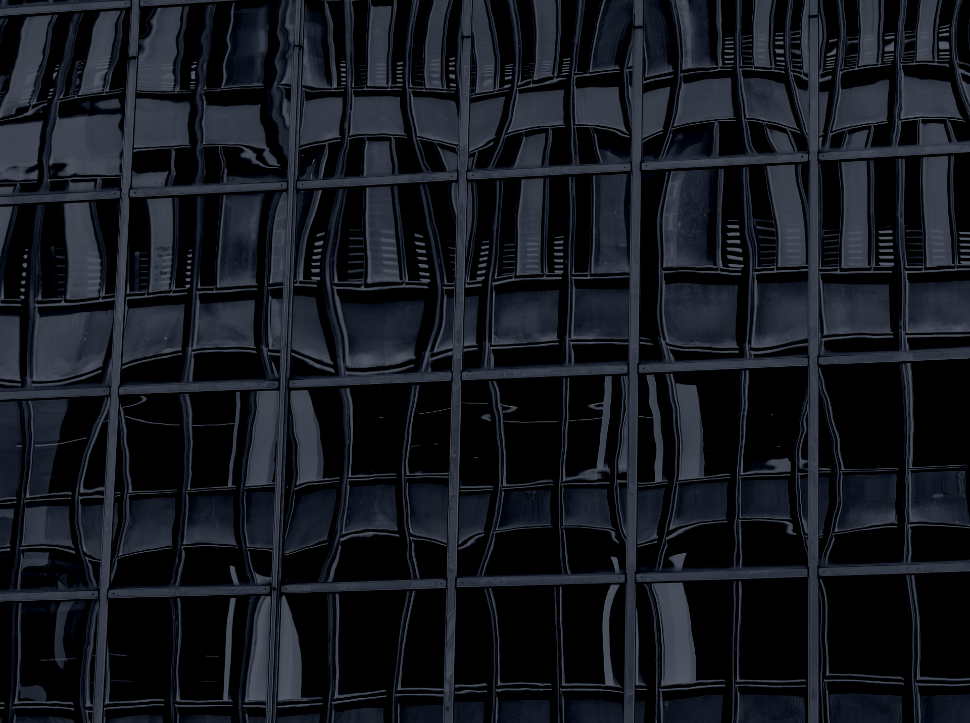 Dark reflective glass windows of a modern Manhattan building showing distorted reflections of architectural elements.