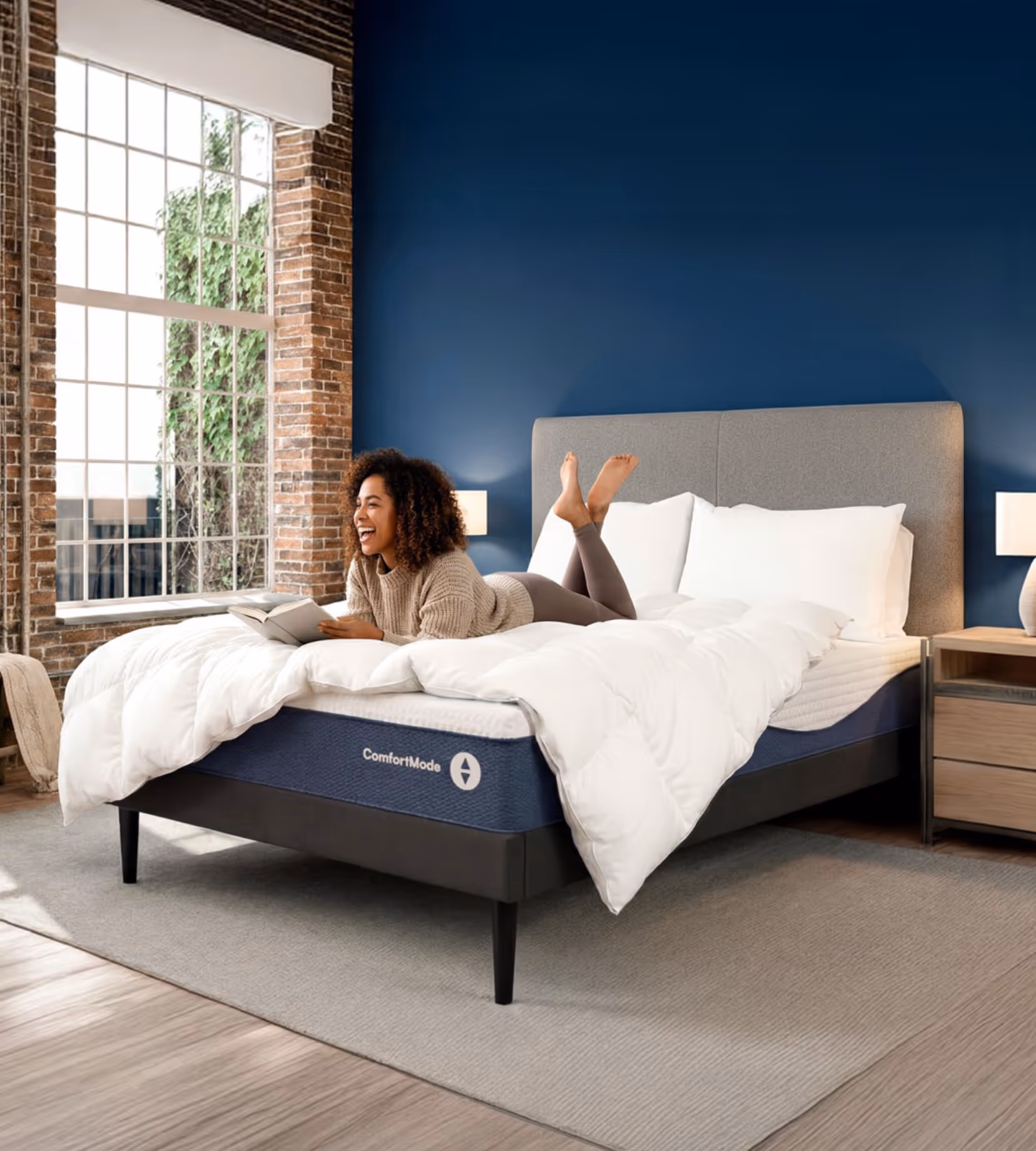 Woman lying on a ComfortMode mattress in a modern bedroom reading a book and smiling.