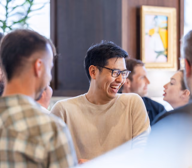 Group of people laughing and talking in a casual indoor setting with framed art on the wall.