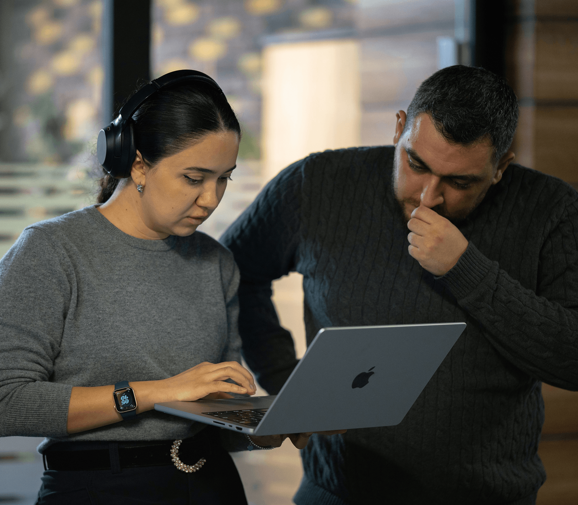 Two people focused on a laptop; one woman types while a man looks thoughtfully at the screen.