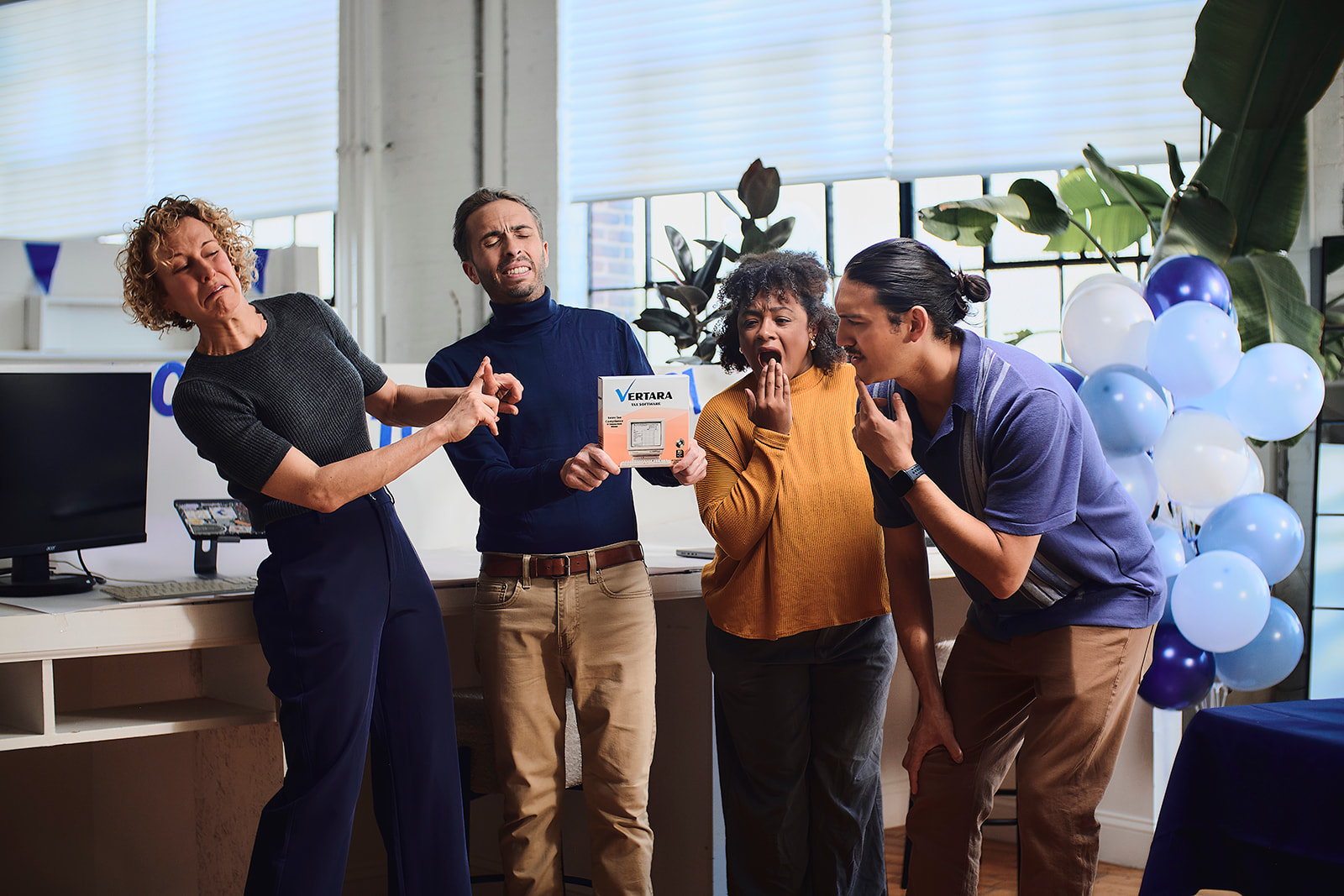Four adults indoors with varied surprised and shocked expressions, one holding a software box labeled Vertara.
