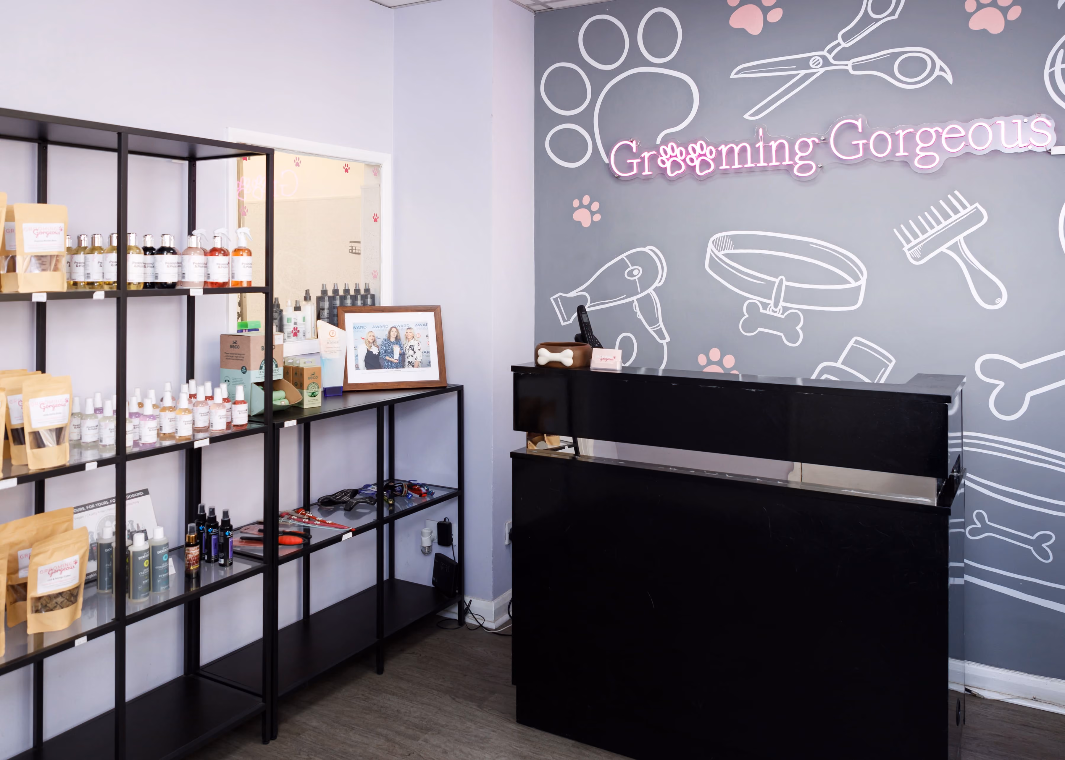Pet grooming reception with black desk, product shelves, and a gray wall with grooming tool drawings and text.