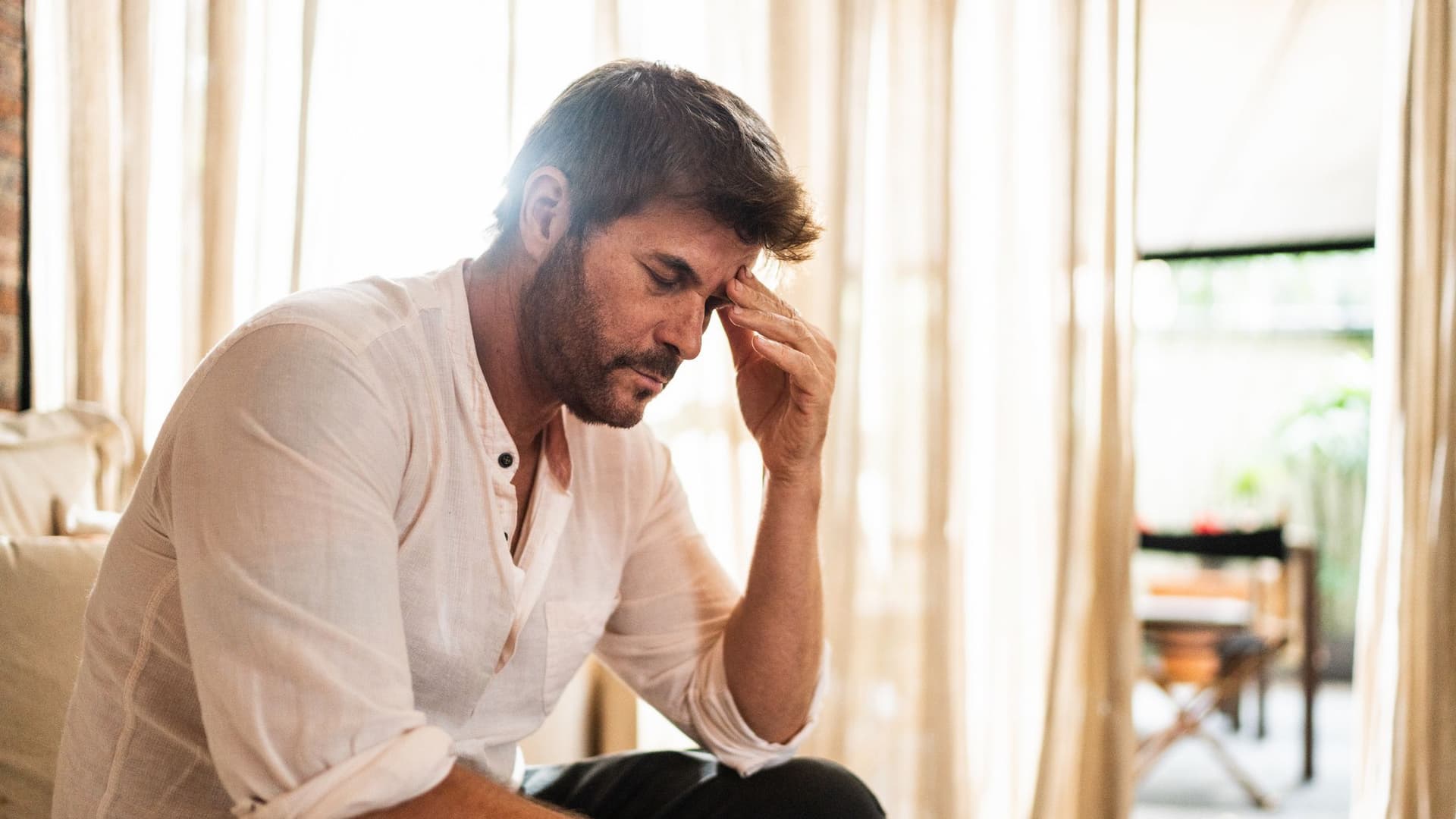 Man sitting on a couch, resting his head in his hands, showing stress or deep contemplation.