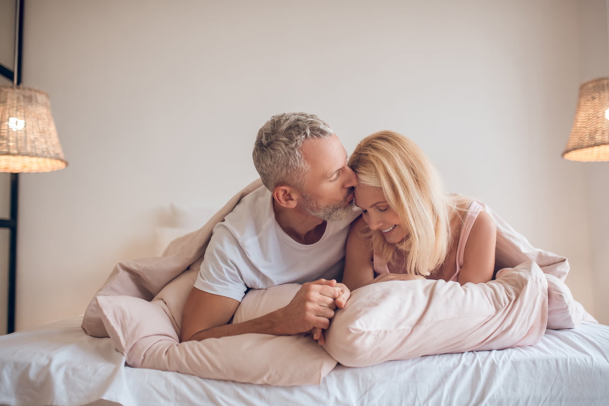 A couple lies in bed together, sharing a quiet moment of intimacy and peaceful connection.