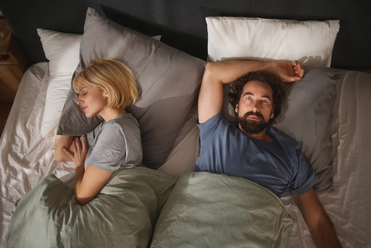 Couple lying in bed back-to-back looking stressed, representing stress and sex, performance anxiety in men, and the impact of stress on sexual health.