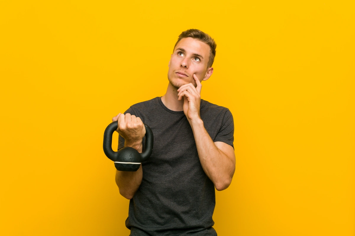 Man holding a kettlebell while thinking, representing lifestyle factors, exercise, and the physical and psychological causes of erectile dysfunction.