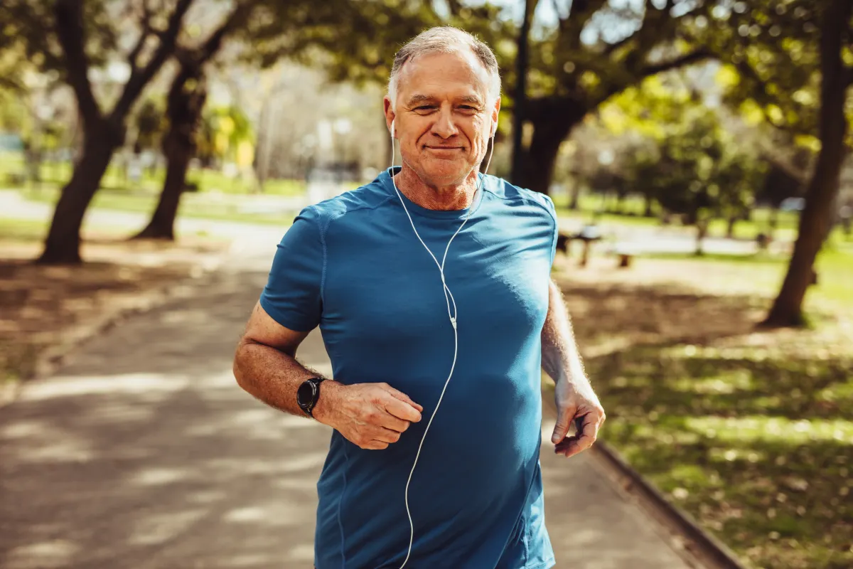 Middle-aged man jogging outdoors wearing earphones as part of a healthy lifestyle routine.