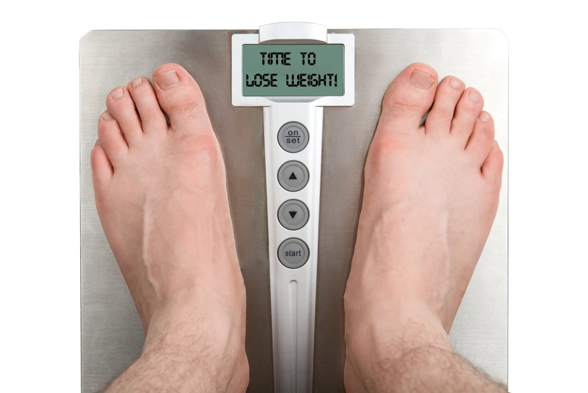 Man standing on a scale to monitor weight loss progress, metabolism changes, and hormone-related fat loss goals in men. 
