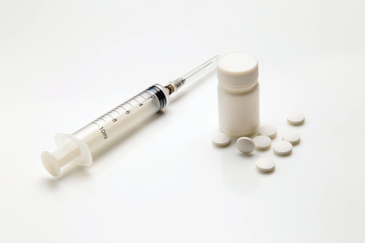 Syringe placed next to a pill bottle and tablets, representing the comparison between TRT injections, gels, and pellets as testosterone replacement therapy delivery options.