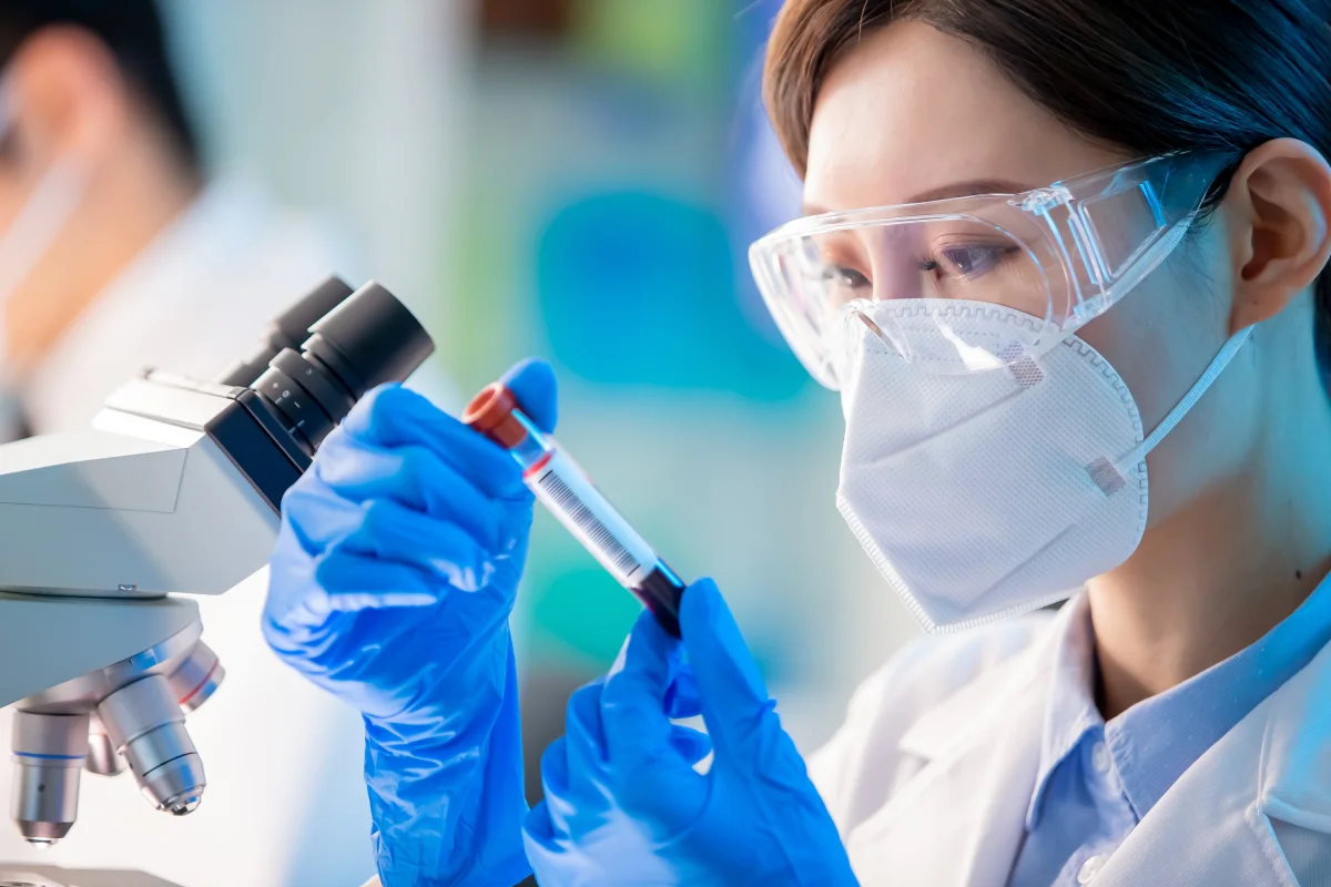 Lab technician holding a blood sample vial under a microscope, representing how testosterone blood tests work to evaluate hormone levels for men's health treatment.
