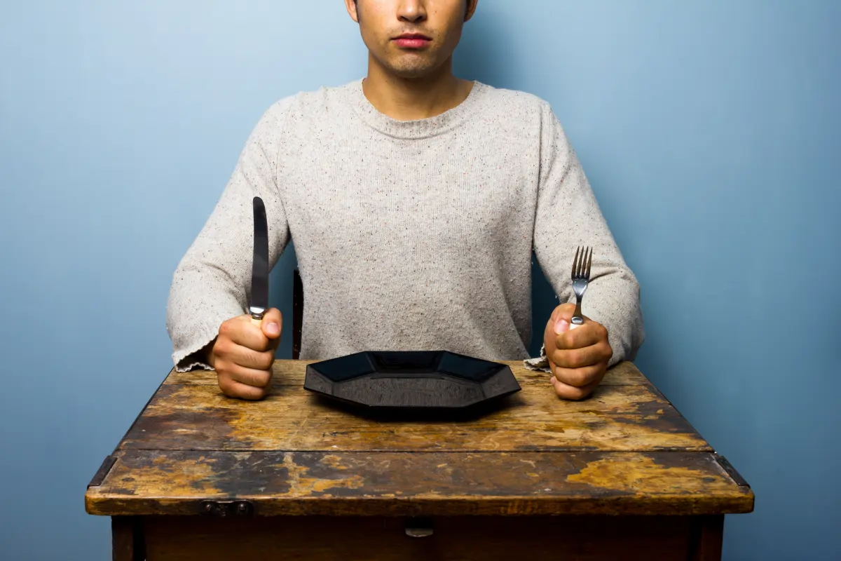 Man sitting at a table with an empty plate to represent intermittent fasting, testosterone health, metabolic benefits, and weight management for men.