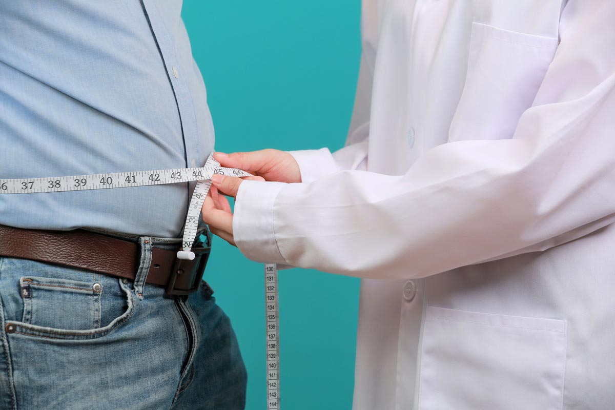 Healthcare provider measuring the waist of a male patient, representing the relationship between testosterone and body fat and the impact of low testosterone symptoms in men on weight and hormone balance.