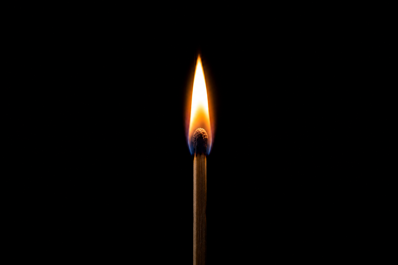 Close-up of a burning matchstick flame against a dark black background.
