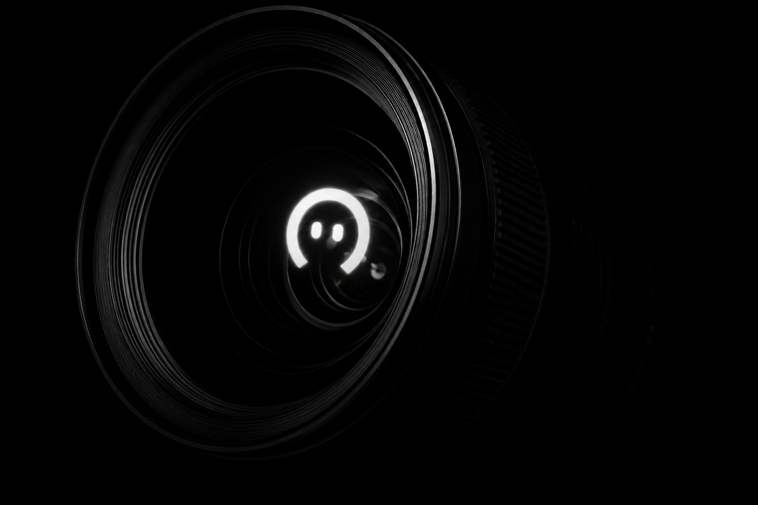 Close-up of a camera lens with a bright reflection in the center against a dark background.